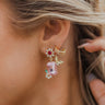 Close side view of model wearing the New Blooms Earrings, that have clear and red rhinestone flowers on post backs with pink rectangular pendants, embellished with leaf and floral rhinestones.
