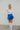 Full body front view of model wearing the Bright Idea Skort, that has royal blue satin fabric, a front skirt overlay with a twist detail, and a back zipper