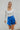 Front view of model wearing the Bright Idea Skort, that has royal blue satin fabric, a front skirt overlay with a twist detail, and a back zipper