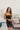 Frontal view of the Icon Mini Dress that features a black colored PU material, a straight neckline, a sleeveless design, a small front slit, and a hidden back zipper.