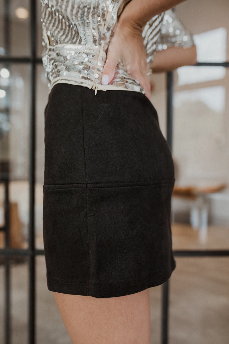 Side view of The Static Radio Skirt In Black features black suede fabric, lining details, mini length, and elastic waistband.