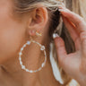 Close side view of model wearing the Fresh Start Earrings, which feature gold hooks and a large teardrop pendant with gold, beige, grey, and white beading.