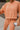 Close-up front view of model wearing the Setting The Vibe Top, which has an orange terry cloth ribbed material, a round neck, long cuffed sleeves, a thick bottom hem, and side slits. Worn with matching pants