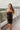 Frontal view of the Icon Mini Dress that features a black colored PU material, a straight neckline, a sleeveless design, a small front slit, and a hidden back zipper.