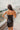 Back view of the Icon Mini Dress that features a black colored PU material, a straight neckline, a sleeveless design, a small front slit, and a hidden back zipper.