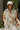 Front view of model wearing the Keep Them Guessing Hooded Vest, that has a green nylon material, a sleeveless design, a button-up front, 2 front hidden pockets, and a heather grey hood. Styled with crossbody purse.