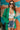 Frontal view of the Blakely Blazer In Green that features a green material, a collar and lapel, a two button front closure, a long sleeve, shoulder pads, two front pockets, and a back slit.