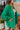 Side view of the Blakely Blazer In Green that features a green material, a collar and lapel, a two button front closure, a long sleeve, shoulder pads, two front pockets, and a back slit.