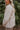 Side view of The Floral Dreams Jacket features cream coloring fabric, flower stitched pattern, two front buttoned chest pockets, cream button up with a collared neckline, two side pockets, and long sleeves with buttoned cuffs.