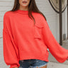 Frontal view of the Walk The Line Sweater that features a red knit material, a round neck, a long sleeve, a front pocket, a high-low design, and a flowy fit.