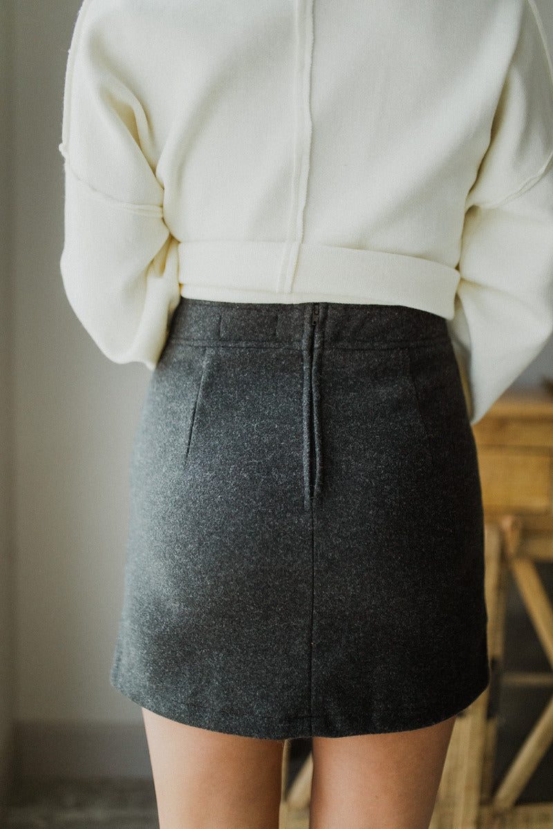 Back view of The All American Skirt In Charcoal features charcoal grey knit fabric, two front pockets, mini length, and back zipper closure.
