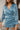 Frontal view of the Every Breath Mini Dress features a blue shimmer material, a surplice neckline, long sleeves with smocked detailing at the wrist, a front ruched detail, a ruched back seam, a back zipper closure, an open back with a button closure, and 