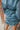 Back view of the Every Breath Mini Dress features a blue shimmer material, a surplice neckline, long sleeves with smocked detailing at the wrist, a front ruched detail, a ruched back seam, a back zipper closure, an open back with a button closure, and a r