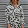 Front view of model wearing the Don't Blend In Top that has cream and black satin fabric with a geometric stripe pattern, a button up front with a collared neckline, and long sleeves with buttoned cuffs.