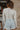 Back view of the See You Around Top that features a white material a high neckline, a long sleeve, lettuce edge hems, and a patchwork design.