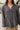 Frontal view of the Bare With Me Top that features a charcoal grey gauze material, a V neckline, a button-up front, a long cuffed sleeve, raw hemlines through out, and side pockets.