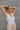 Front view of model wearing the Play It Cool Bodysuit that has white ribbed fabric, a v-neckline, a sleeveless body, a thong bottom and hook closures.