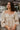 Frontal view of the love You More Top that features a champagne colored silk material, a straight neckline with a tie detail, a long sleeve, a pleated front, a smocked back, a back zipper closure, and a flowy fit.