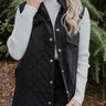 Close up of The All That She Wants Vest features black color fabric, quilted pattern, two front chest pockets, two side pockets, mini length, slits on each side, button up, collared neckline and sleeveless.