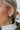 Close up view of model wearing the All Season Long Earrings which features embellished green and gold beads, floral pattern on a closed hoop.