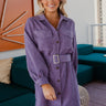 Frontal view of the Purple Haze Corduroy Dress that features a purple corduroy material, a long cuffed sleeve, a collar neck, a button-up front, two front pockets, an adjustable belt, and a mini length.
