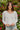 Frontal view of the Wandering Minds Top that features a white cotton material, a V neckline, a long sleeve, a babydoll design, and a flowy fit.