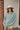 Frontal View Line Of Sight Top that features a sage green gauze material, a collar neck, a button-up front, a long cuffed sleeve, two front pockets, and frayed raw hemlines.
