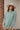 Frontal View Line Of Sight Top that features a sage green gauze material, a collar neck, a button-up front, a long cuffed sleeve, two front pockets, and frayed raw hemlines.