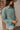 Side View Line Of Sight Top that features a sage green gauze material, a collar neck, a button-up front, a long cuffed sleeve, two front pockets, and frayed raw hemlines.