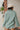 Back View Line Of Sight Top that features a sage green gauze material, a collar neck, a button-up front, a long cuffed sleeve, two front pockets, and frayed raw hemlines.