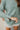 Frontal View Line Of Sight Top that features a sage green gauze material, a collar neck, a button-up front, a long cuffed sleeve, two front pockets, and frayed raw hemlines.