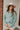 Frontal View Line Of Sight Top that features a sage green gauze material, a collar neck, a button-up front, a long cuffed sleeve, two front pockets, and frayed raw hemlines.