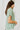 Side view of model wearing the Can't Go Wrong Top, which has a sage green colored material, a collar neck, a button-up front, a short cuffed sleeve, a front pocket, and a flowy fit