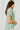 Side view of model wearing the Can't Go Wrong Top, which has a sage green colored material, a collar neck, a button-up front, a short cuffed sleeve, a front pocket, and a flowy fit