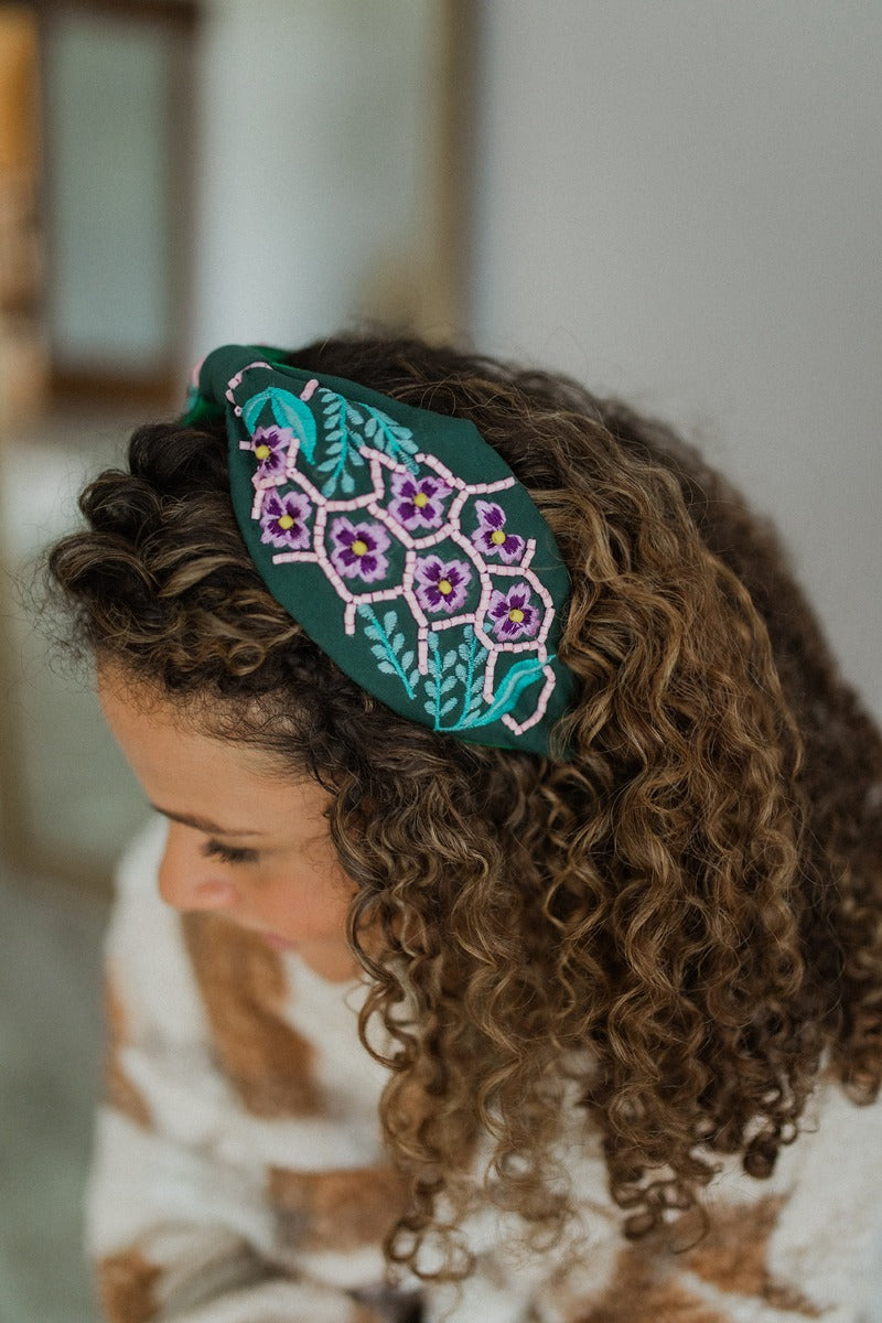 Aerial view of model wearing the Flower Power Headband which features emerald coloring fabric, turquoise and purple stitching, floral pattern with pink and yellow beads.