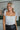Front view of model wearing The Angel Baby Feather Top features a white silk material, a sleeveless design with thin straps, feather detailing on the straps, a cowl neckline, and a flowy fit.