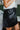 Side view of the Enough For Me Skirt that features a black colored PU material, a cross-over front design, a front panel with an adjustable tie, a back elastic band waist, and a mini length.