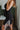 Side view of model wearing The Starlight Rhinestone Fringe Dress features a black colored material, a straight neckline, a sleeveless design with thin adjustable straps, rhinestone fringe detailing at the bottom side hem, criss cross straps in the back, a