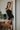 Front view of model wearing The Starlight Rhinestone Fringe Dress features a black colored material, a straight neckline, a sleeveless design with thin adjustable straps, rhinestone fringe detailing at the bottom side hem, criss cross straps in the back, 