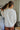 Back view of the Perfect Timing Top that features an ivory colored material, a collar neck, a 3/4 button-up, a long sleeve, two front pockets, and an oversized fit.