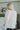 Back view of the Easy Breezy Top that features a cream colored knit material, an open knit design, a V neckline, a long cuffed sleeve, side slits, and a high-low design.