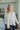Frontal view of the Easy Breezy Top that features a cream colored knit material, an open knit design, a V neckline, a long cuffed sleeve, side slits, and a high-low design.
