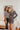 Frontal view of the Bring It Back Mini Dress that features a black colored material, a white plaid pattern, a collar and lapel neckline, a long sleeve, an open front with a clasp closure, waist cut-outs, a tie detail at the waist, a side slit, and a side 