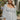 Frontal view of the Pocket Full Of Sunshine Top that features a white chiffon material, a black flower print, a sweetheart neckline, a long sleeve, a babydoll silhouette, and a smocked back.