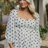 Frontal view of the Pocket Full Of Sunshine Top that features a white chiffon material, a black flower print, a sweetheart neckline, a long sleeve, a babydoll silhouette, and a smocked back.
