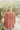 Back view of the Easy Breezy Top that features a pink colored knit material, an open knit design, a V neckline, a long cuffed sleeve, side slits, and a high-low design.