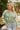 Front view of model wearing Matcha Daisy Cardigan features a green knit material, a white flower print, long sleeves, and a button-up front closure.