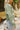 Side view of model wearing Matcha Daisy Cardigan features a green knit material, a white flower print, long sleeves, and a button-up front closure.