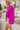 Side view of model wearing the Take Me Out Top, which features a purple colored material, a collar V neck with a button, a long flowy sleeve with a smocking at the wrist, a draped bottom hem. Tucked into beige skirt.