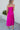 Full body back view of model wearing the Let's Dance Midi Dress, which features a fuchsia satin material, a cowl neckline, a sleeveless design with thin adjustable straps, a side slit, and a midi length.